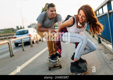 Porträt eines glücklichen Paares, das Spaß beim Fahren eines langen Brettes in der Stadt hat. Menschen Skateboard Konzept Stockfoto