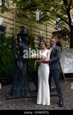 Ukrainische Jungvermählte posieren für ein Bild der Pronya Prokopivna und Svirid Holokhvastov Skulptur auf Andriivskyi Abstieg in Kiew, Ukraine. Stockfoto