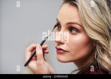 Sie zieht es vor, an ihrem großen Tag ihr eigenes Make-up zu machen. Ausgeschnittene Aufnahme einer schönen jungen Braut, die sich schminkt, während sie sich auf ihre Hochzeit in ihr vorbereitet Stockfoto