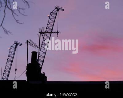 Eine lebendige, reiche Morgendämmerung über London, mit Kräne, Schornsteintöpfen und Antennen, die vor einem violetten, rosa und roten Himmel silhouettiert werden. Stockfoto