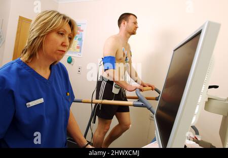 Eine Kardiologin überwacht die Bildschirmanzeige, während ihre Patientin auf dem am EKG befestigten Laufband joggt. (MODELL FREIGEGEBEN) Stockfoto