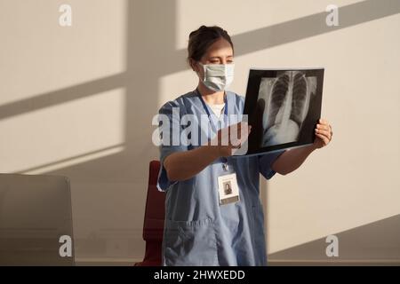 Junge ernsthafte Radiologin, die sich das Röntgenbild nach einer radiologischen Untersuchung des Patienten im Stehen in der Arztpraxis ansieht Stockfoto