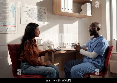 Junge kranke Patientin und ein Arzt diskutieren Möglichkeiten der medizinischen Behandlung von Krankheiten, während sie vor einander sitzen Stockfoto