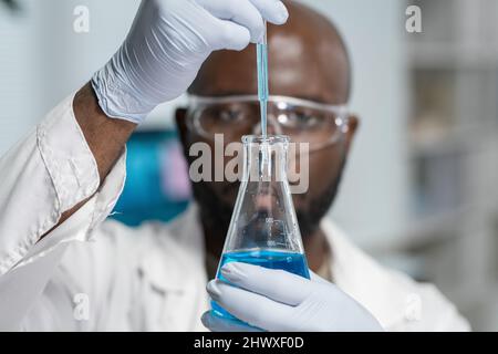 Handschuhen eines modernen Chemikers mit Pipette, die während des wissenschaftlichen Experiments flüssige Substanz in das Röhrchen tropft Stockfoto