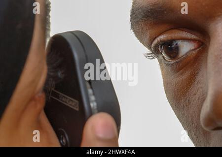 Ein Hausarzt, der das Auge eines jungen Mannes mit einem Ophthalmoskop untersucht (MODEL RELEASE). Stockfoto