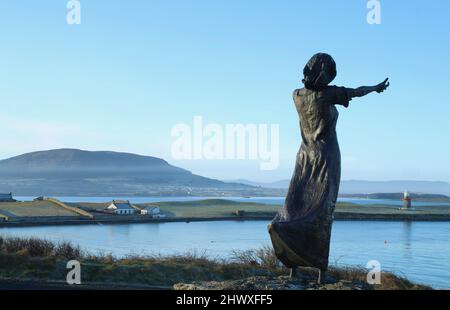 Blick von hinten Silhouette der Statue über Kanal auf Oyster Island mit Bergen im Hintergrund. Rosses Point, Sligo, Irland Stockfoto