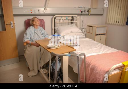 Eine ältere Dame an ihrem Bett in einer Krankenstation. (MODEL VERÖFFENTLICHT) Stockfoto