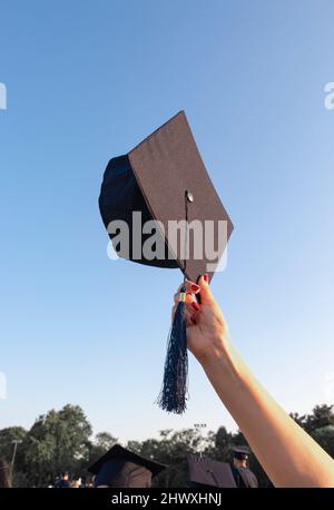 Die Abschlusskappe hält sich am blauen Himmel fest. Das Konzept von stolz, Ehre, Erfolg. Stockfoto