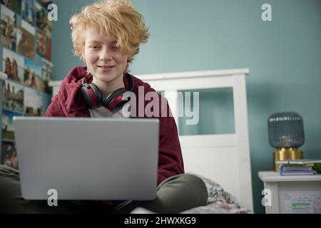 Teenager-Mädchen Mit Kabellosen Kopfhörern, Die Auf Einem Laptop Arbeiten, Im Schlafzimmer Zu Hause Stockfoto