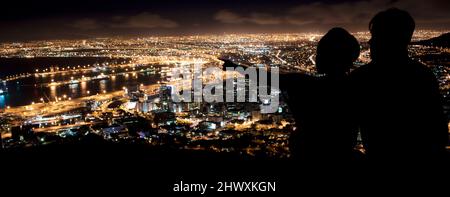 Der beste Platz im Haus. Silhouette eines jungen Paares, das die nächtliche Landschaft der Stadt genießt. Stockfoto