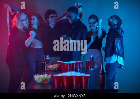 Eine vielfältige Gruppe von Menschen, die bei einer Party in Neonlicht Spiele spielen und Spaß haben Stockfoto