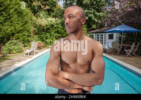 Ein junger, sportlich aussehender Mann, der vor einem Schwimmbad steht. -(MODELL FREIGEGEBEN) Stockfoto