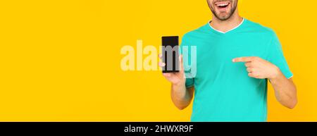 Zugeschnittenes Mann präsentiert Telefonbildschirm. Guy zeigen Finger auf Smartphone auf gelbem Hintergrund. Stockfoto