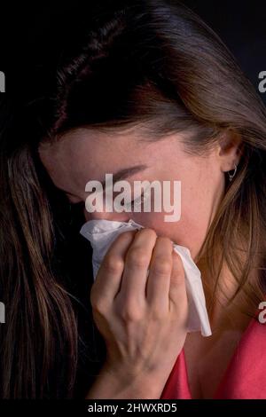 Junge Frau niest in ein Gewebe (MODELL FREIGEGEBEN)