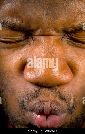 Ein junger Mann drückt seine Augen zu und drückt seine Lippen fest zu (MODEL FREIGEGEBEN) Stockfoto