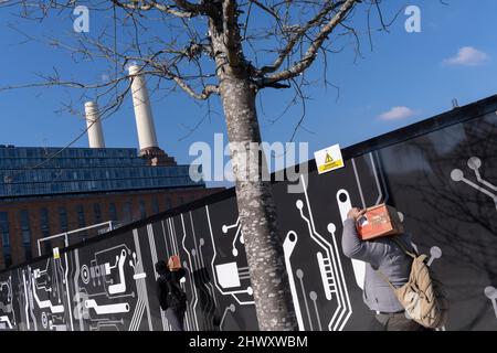 Zwei Arbeiter tragen ähnliche Kisten aus der Bauindustrie am 7.. März 2022 in London, England, in Richtung Battersea Power Station auf der Pump House Lane in Nine Elms. Stockfoto