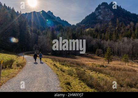 Zwei Frauen gehen an einem sonnigen Tag im Spätherbst auf einer kurvenreichen Schotterstraße zwischen Feldern und Bergen in der Schwarzee-Region des Kantons Freiburg in der Schweiz. Hochwertige Fotos Stockfoto