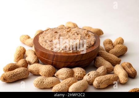 Amerikanisches Frühstück, süße Speisen und Snacks mit hohem Kalorien-Konzept mit einer Schüssel knackige Erdnussbutter von Erdnüssen noch in Schale, isoliert umgeben Stockfoto