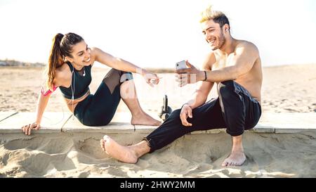 Glückliches Paar, das beim Sport-Fitnesstraining Pause macht und die Geschichte auf dem Handy teilt - Technologie-Sportkonzept mit jungen Sportlern enjoyi Stockfoto