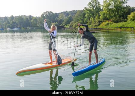 Zwei junge Leute haben Spaß beim Paddeln mit einem SUP-Board auf einem See Stockfoto
