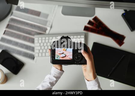 Nahaufnahme einer Fotografin, die die Kamera mit dem Bild auf dem Bildschirm hält, während sie am Arbeitsplatz Fotos bearbeitet Stockfoto