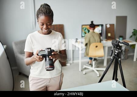Porträt einer lächelnden afroamerikanischen Frau, die die Kamera hält, während sie im Fotostudio arbeitet, Kopierraum Stockfoto