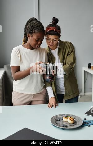 Vertikales Porträt von zwei weiblichen Fotografen, die Fotos in der Kamera betrachten, während sie im Fotostudio arbeiten Stockfoto
