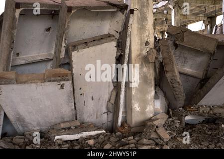 Ein Haufen grauer Betonplatten der Überreste des Gebäudes in Nahaufnahme vor dem Hintergrund des Rahmens des zerstörten Gebäudes. Hintergrund. Stockfoto