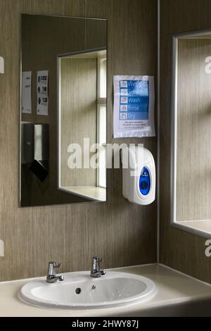 Waschräume oder WC-Innenraum (Waschbecken, 2 heiß- und Kaltwasserhähne, Handwäsche-Beratung Erinnerung, Reflexion im Spiegel,) - Bolton Abbey, Yorkshire, England, UK. Stockfoto