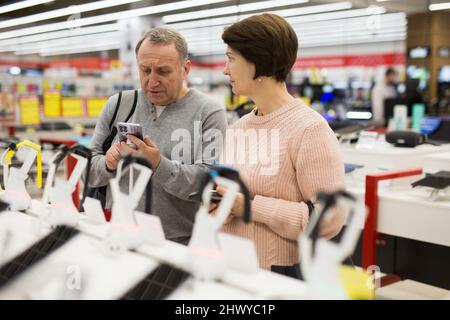 Ehefrau und Ehemann mittleren Alters pflücken neues Smartphone im Elektronikgeschäft Stockfoto