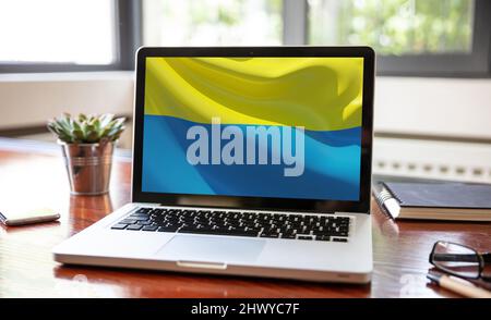 Unterstützen Ukraine, spenden helfen ukrainischen Menschen. Flagge auf Computer-Laptop-Bildschirm. Hintergrund des Büroschreibtisches Stockfoto