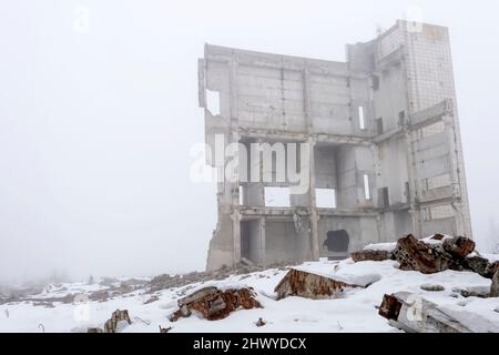 Die Überreste eines konkreten Gebäudes in einer nebligen Dunst mit Fragmenten der Struktur in den Vordergrund, mit Schnee bedeckt. Hintergrund. Für Text platzieren. Stockfoto