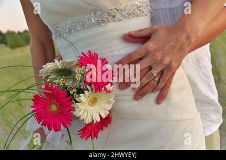 Nahaufnahme des Bräutigams, der seine Arme um die Taille der Braut legt, mit Eheringen, Kleid und Blumenstrauß Stockfoto