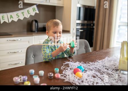 Fokussierter kreativer Junge, der Eier zu Ostern schmückt Stockfoto