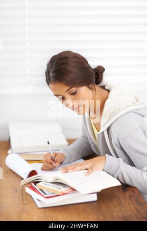Funkennoten absenken. Seitenansicht einer jungen Studentin, die sich Notizen aus ihrem Lehrbuch gemacht hat. Stockfoto
