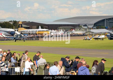 Zweiter Weltkrieg Bearcat-Kampfflugzeug rollt während einer Flugshow am IWM Duxford vorbei. Flugzeuge und Hangars hinter dem Publikum Stockfoto