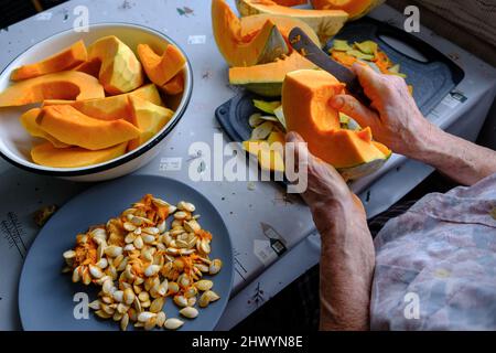 Alte Frau schneidet und Pillen gelben Kürbis, Kochen Kürbissuppe, Ruhestand Leben, selektive Konzentration Stockfoto