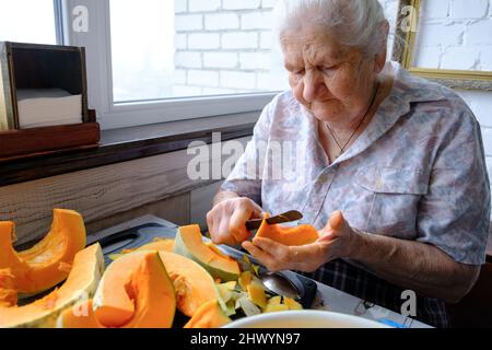 Alte Frau schneidet und Pillen gelben Kürbis, Kochen Kürbissuppe, Ruhestand Leben, selektive Konzentration Stockfoto