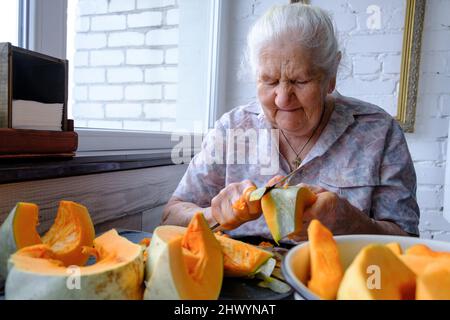 Alte Frau schneidet und Pillen gelben Kürbis, Kochen Kürbissuppe, Ruhestand Leben, selektive Konzentration Stockfoto