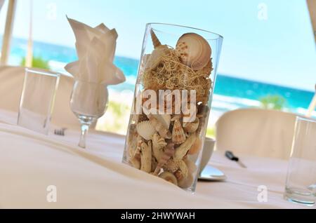 Glasvase im Mittelpunkt, gefüllt mit einer Vielzahl von Muscheln für eine Hochzeit am Strand Stockfoto