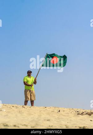 Die Flagge von Bangladesch wird von einem Mann geschwenkt, der Erfolg feiert. Eine schöne Aussicht auf die rote und grüne Flagge (die Nationalflagge von Bangladesch). Stockfoto