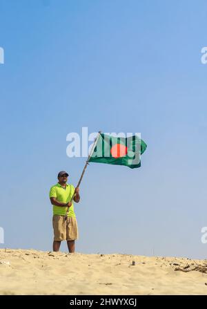 Die Flagge von Bangladesch wird von einem Mann geschwenkt, der Erfolg feiert. Eine schöne Aussicht auf die rote und grüne Flagge (die Nationalflagge von Bangladesch). Stockfoto