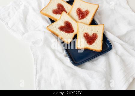 Toast, auf dem das Herz aus Marmelade besteht. Überraschungsfrühstück im Bett. Romantik zum Valentinstag, ein Ort für eine Inschrift Stockfoto