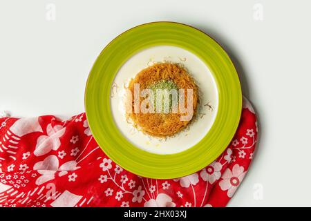 Türkisches Dessert kunefe, kunafa, kadayif mit Pistazie mit Walnusspulver in einer Schale isoliert auf buntem Tischtuch Draufsicht auf grauem Hintergrund Stockfoto