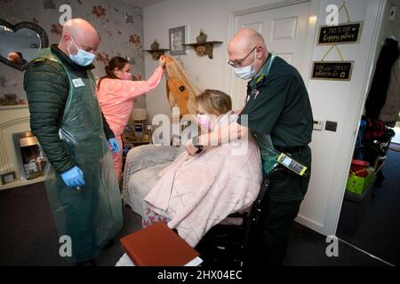 Sanitäter bereiten sich darauf vor, einen Patienten in ihren Krankenwagen zu bringen, nachdem sie den Patienten in ihrem Haus in der Nähe von Pontypool, S. Wales, Großbritannien, untersucht haben Stockfoto