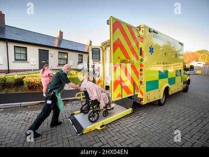 Sanitäter bringen einen Patienten in ihren Krankenwagen, nachdem er den Patienten in seinem Haus in der Nähe von Pontypool, S. Wales, Großbritannien, untersucht hat Stockfoto