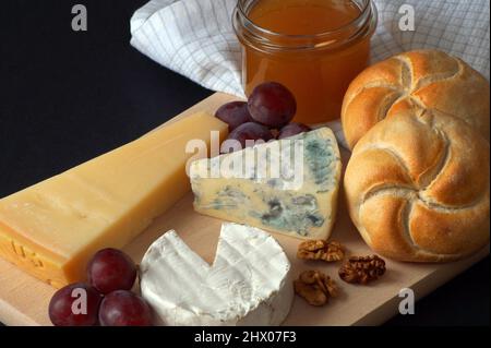 Käseplatte bestehend aus Camembert-Käse, Blauschimmelkäse und Parmesan mit Honig, Trauben, Nüssen und frisch gebackenen Weizenbrötchen Stockfoto