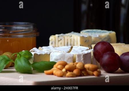 Verschiedene ​​cheeses, Honig, Nüsse, Oliven, Basilikumblätter auf einem Holzbrett gestapelt Stockfoto