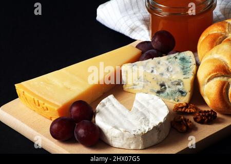 Camembert Brie, Camembert Blue und Parmesan mit Honig und Trauben auf einem Holzbrett Stockfoto