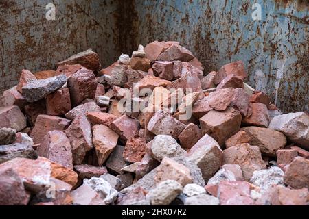 Zerbrochene rote Ziegelsteine aus abgerissenen Mauern im Bauabfallbehälter Stockfoto